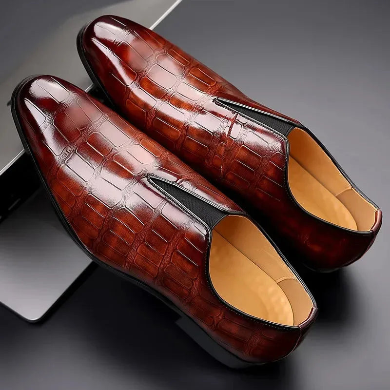 Top-down view of a pair of dark brown croc-embossed loafers resting on a dark reflective surface