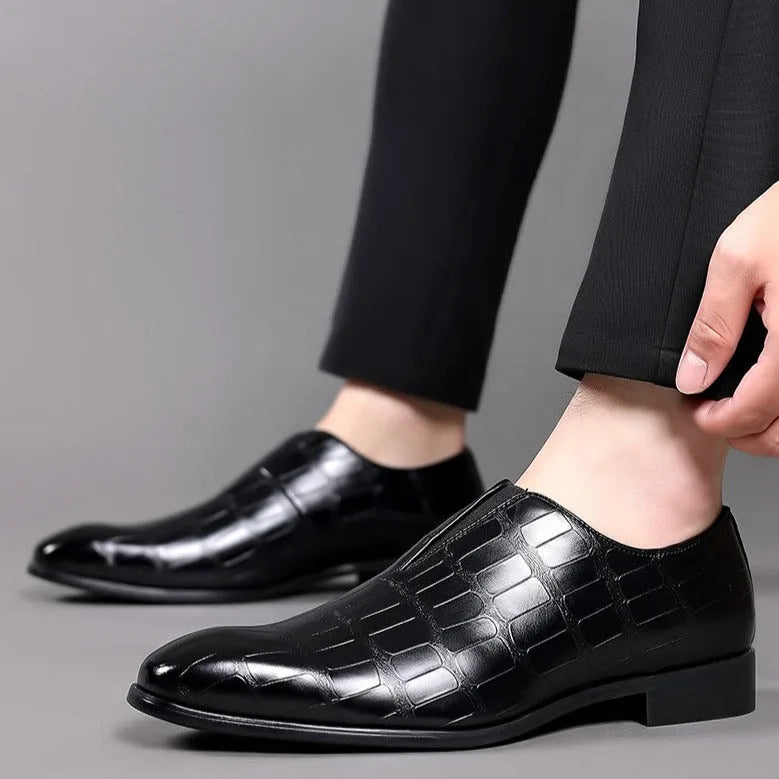 Close-up side view of black croc-embossed loafers on a model's feet paired with black trousers