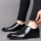 Close-up side view of black croc-embossed loafers on a model's feet paired with black trousers