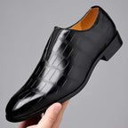 Single dark brown croc-embossed loafer held in hand, showing the pointed toe and slip-on elastic gusset