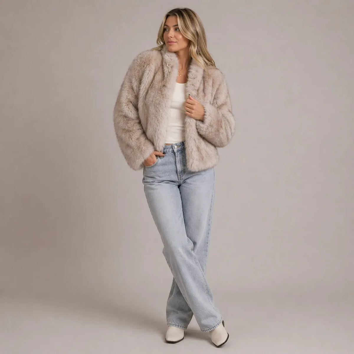 Front view of a woman wearing a taupe faux fur cropped jacket open over a white top and light wash jeans