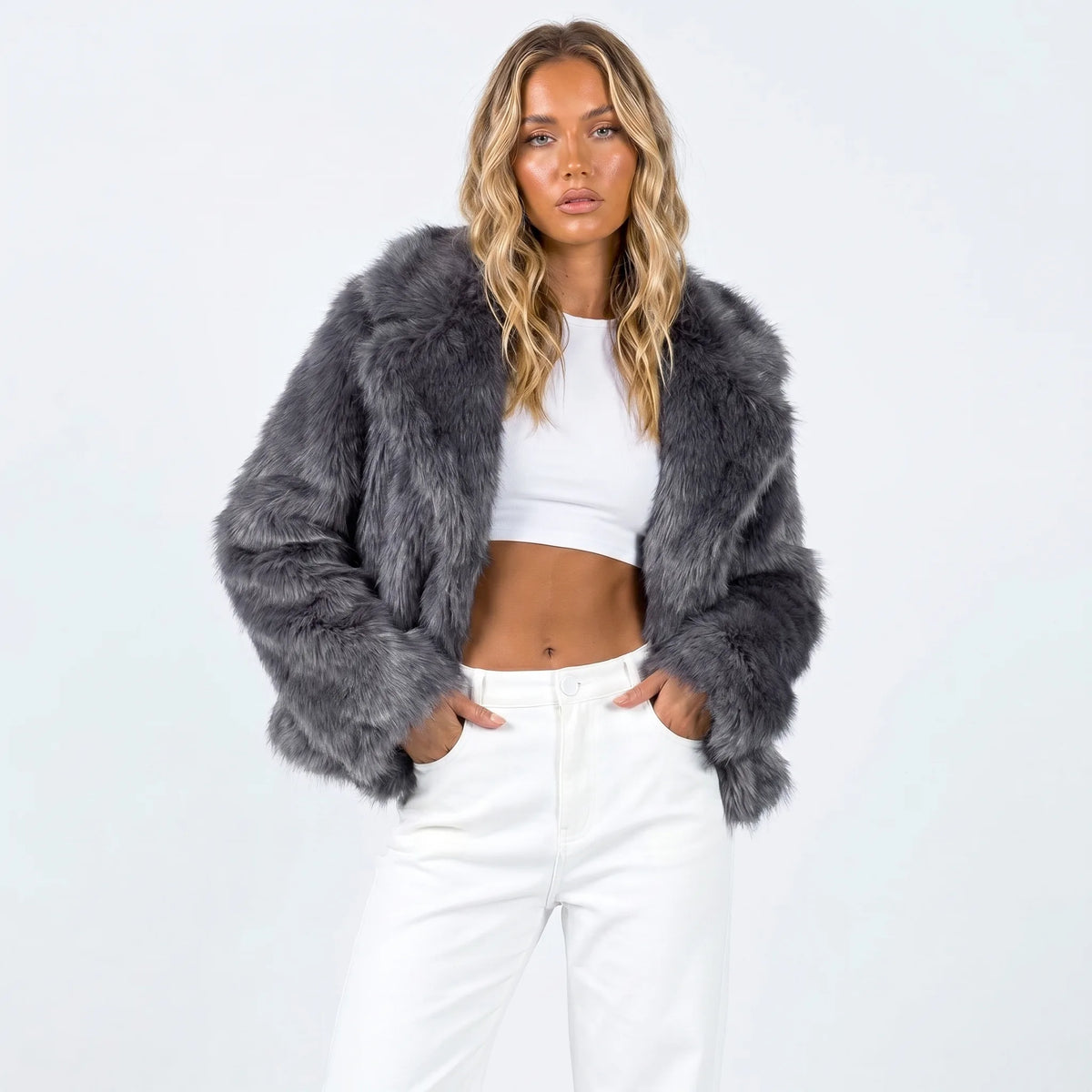 Model wears a cropped faux fur jacket in charcoal grey with wide shawl collar, hands in pockets