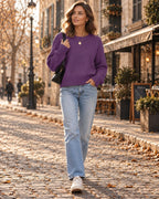 Close view of a purple crew neck jumper with raglan sleeves styled with jeans and a black shoulder bag