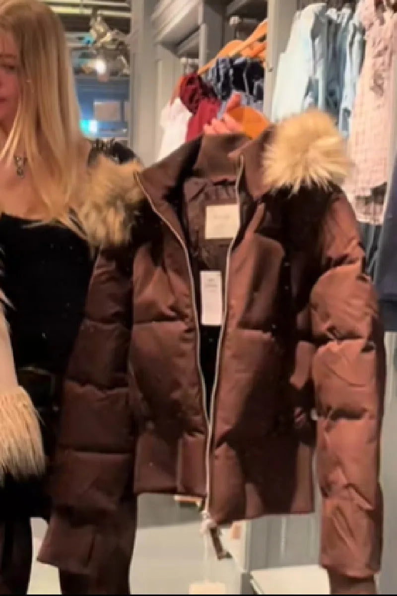 Brown quilted cropped puffer jacket with tan faux fur hood shown on a hanger in a shop display.