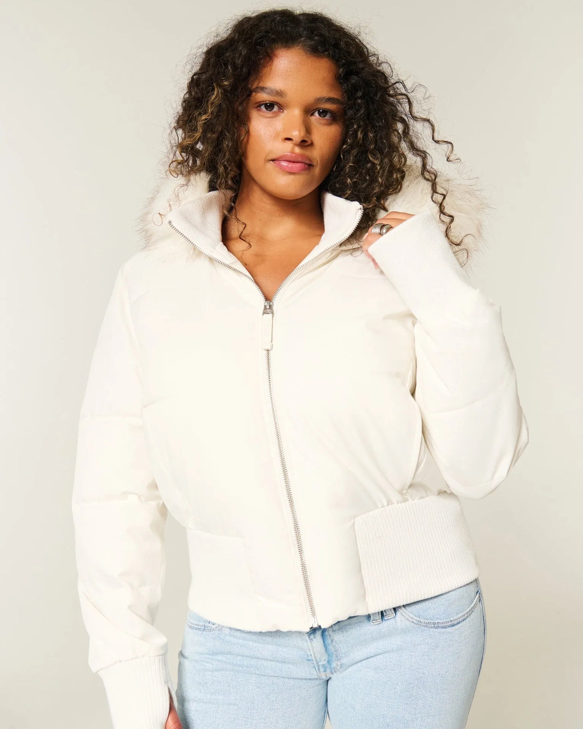 Close-up front view of the cream cropped puffer jacket showing the silver zip, quilted panels and ribbed waistband.