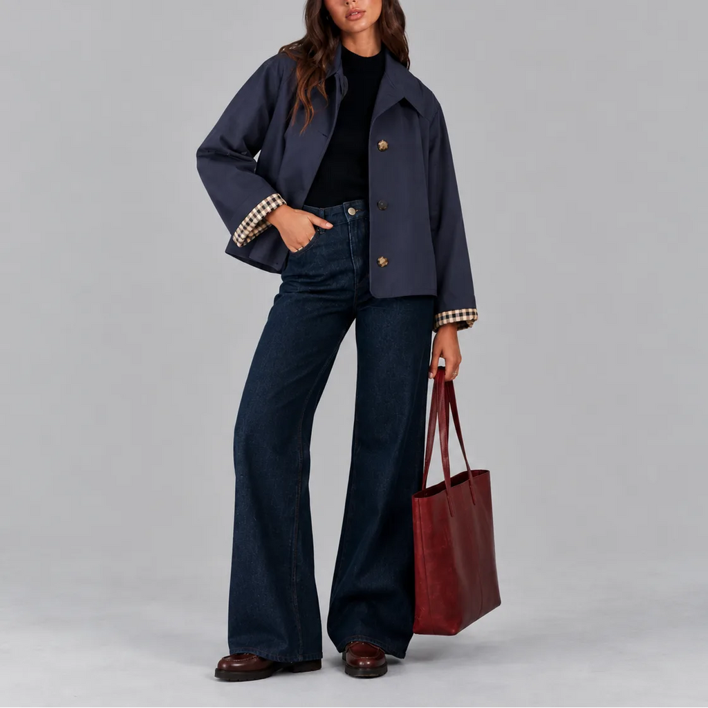 Front view of the navy cropped jacket with tortoiseshell buttons, worn open over a black jumper and dark denim
