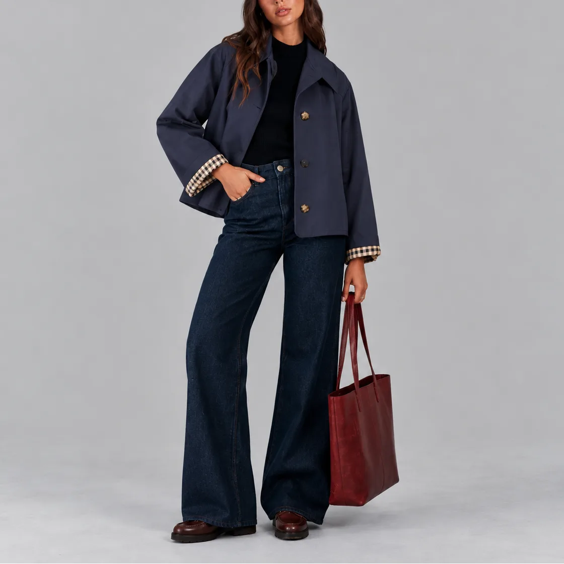 Front view of the navy cropped jacket with tortoiseshell buttons, worn open over a black jumper and dark denim