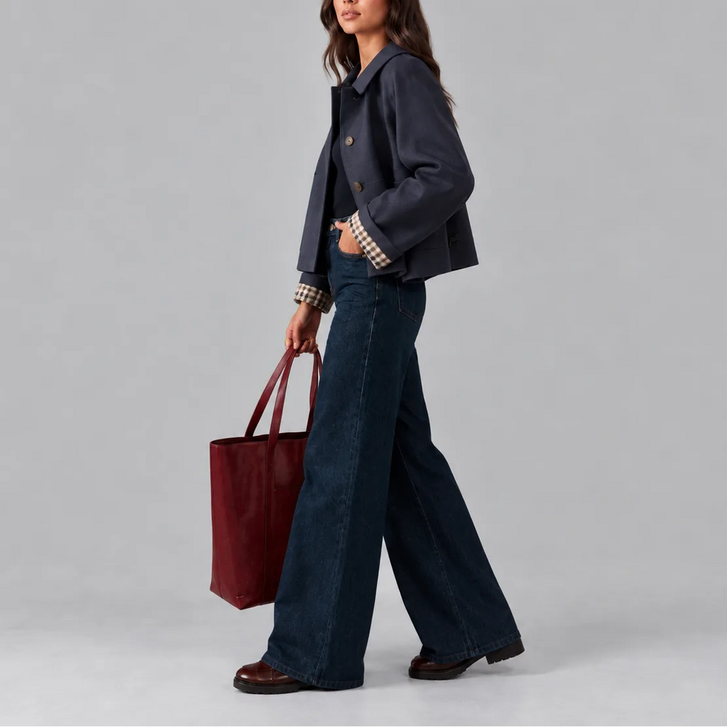 Side profile of the navy cropped jacket, showing its relaxed fit and checked cuff detail while walking