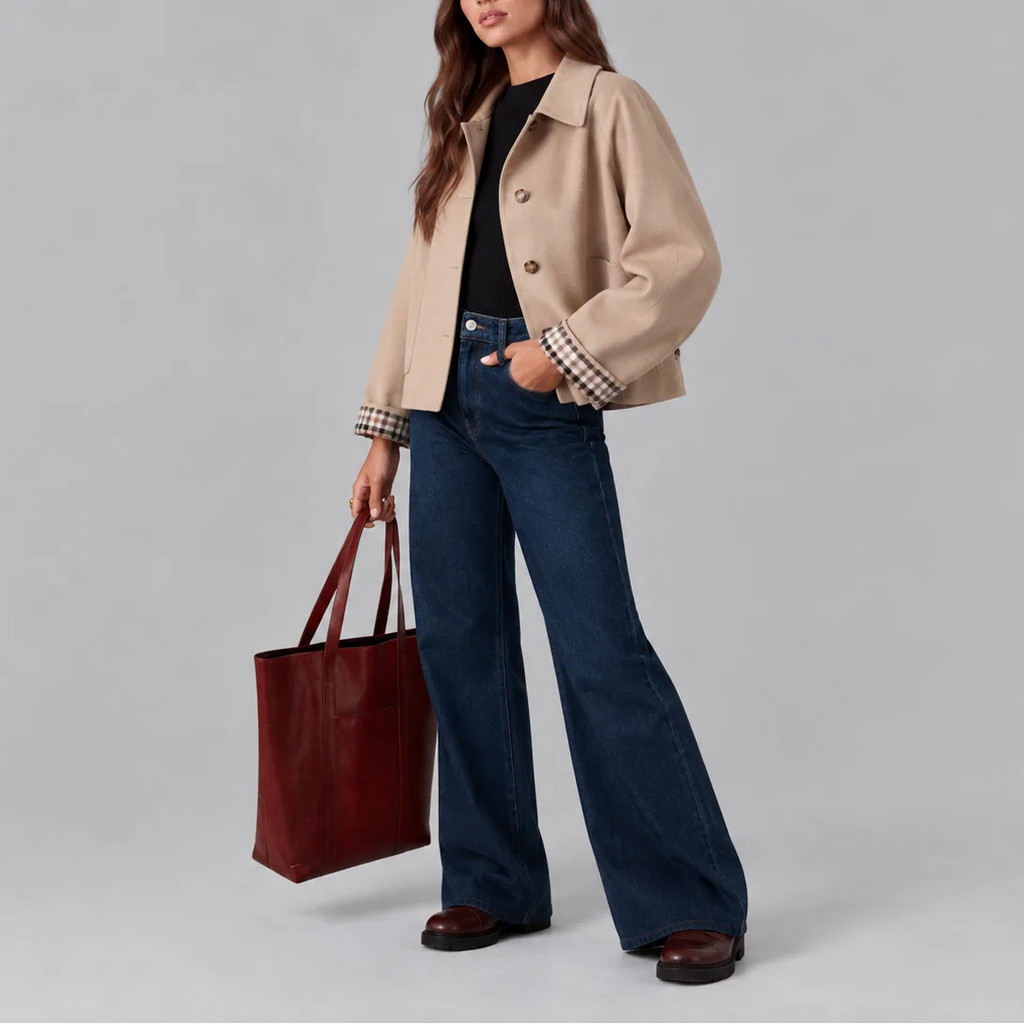 Side view of the beige cropped jacket worn open over a black jumper, styled with denim and a leather tote