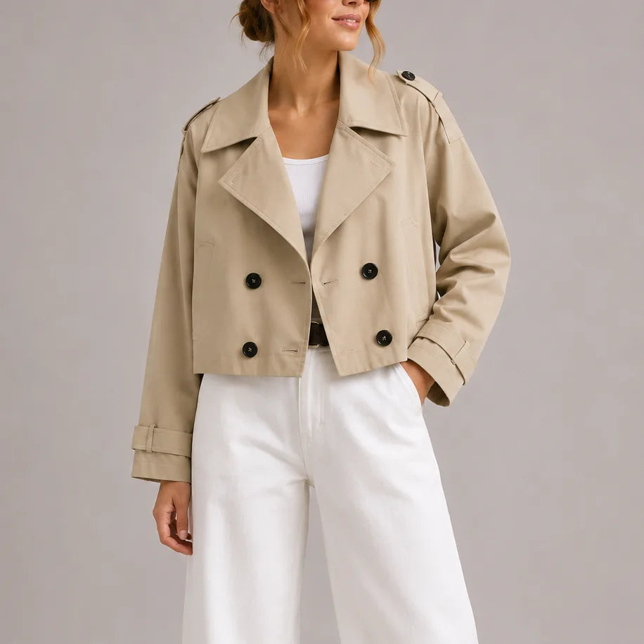 Front view of a beige cropped double-breasted trench jacket with statement lapels styled with white wide-leg trousers