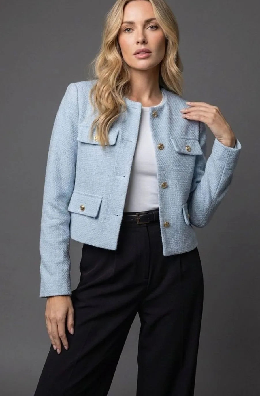 Woman wearing a pale blue textured tweed cropped jacket with gold buttons over a white top and black trousers