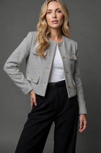 Close-up detail of gold button fastenings on the collarless neckline of the tweed cropped jacket