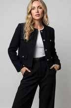 Model in a black textured tweed cropped jacket, collarless, worn open over a white top with black trousers