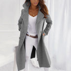 Grey double-breasted mid-length coat with wide lapels, styled over a white blouse and cream trousers