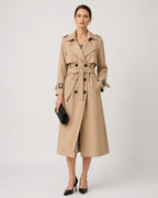 Woman wearing a beige belted trench coat over a checked dress with black heeled shoes, styled for the city
