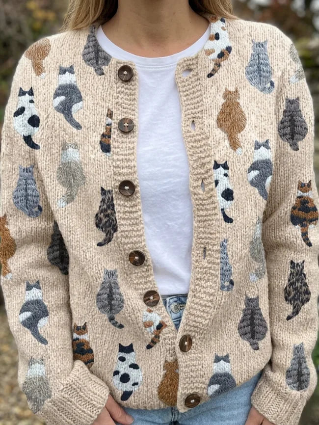 Close-up front view of a cream knit cardigan with embroidered cat motifs, worn open over a white t-shirt and buttoned with brown buttons.