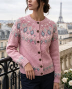 Close-up of a woman on a Paris balcony wearing a pink fair isle yoke cardigan with dusty blue and cream diamond patterning and wooden buttons