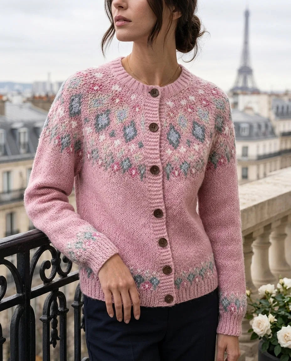 Close-up of a woman on a Paris balcony wearing a pink fair isle yoke cardigan with dusty blue and cream diamond patterning and wooden buttons