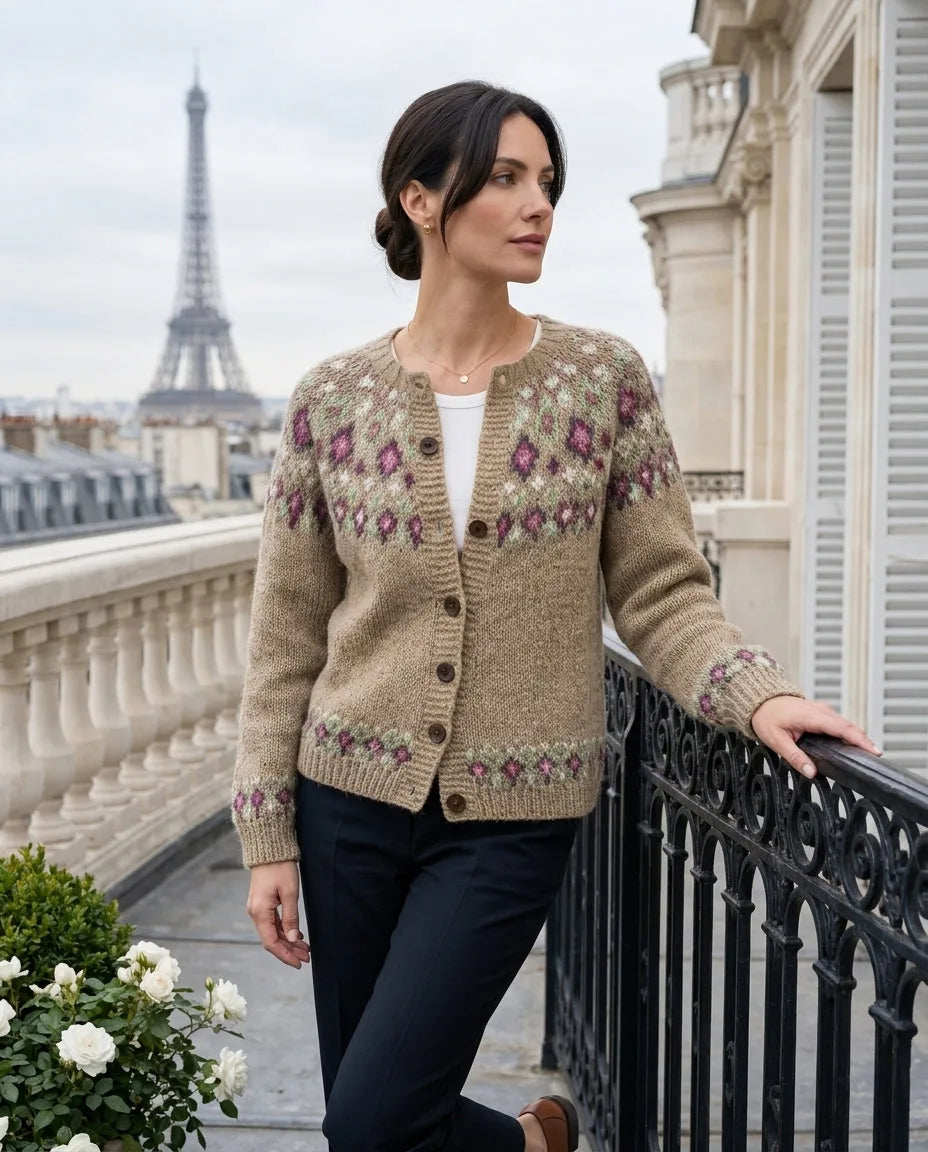 Woman in a camel fair isle cardigan with purple and green floral yoke pattern, leaning on a balcony railing with the Eiffel Tower behind her