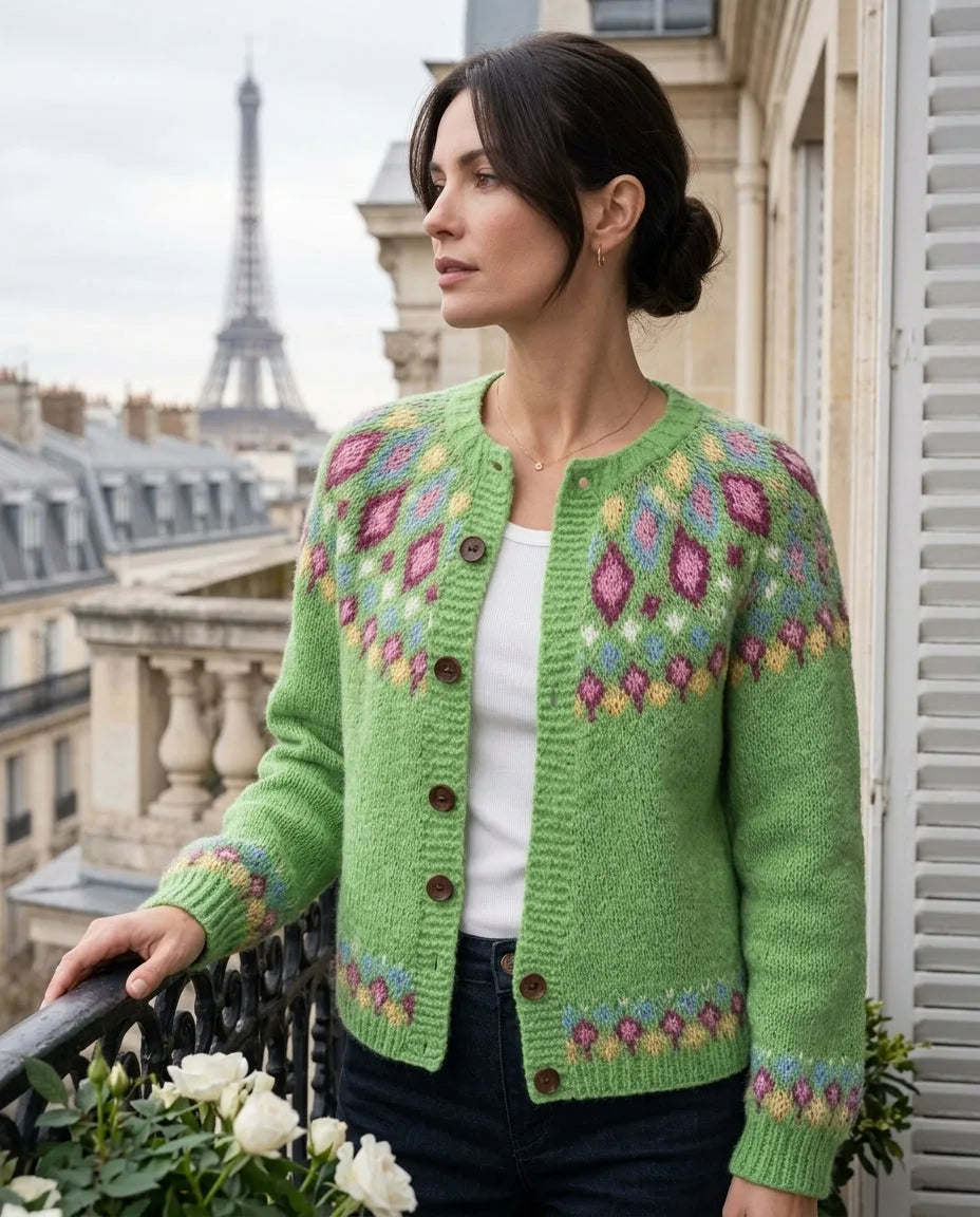 Woman wearing a light green fair isle cardigan with pink, blue and yellow diamond patterned yoke, standing on a Parisian balcony