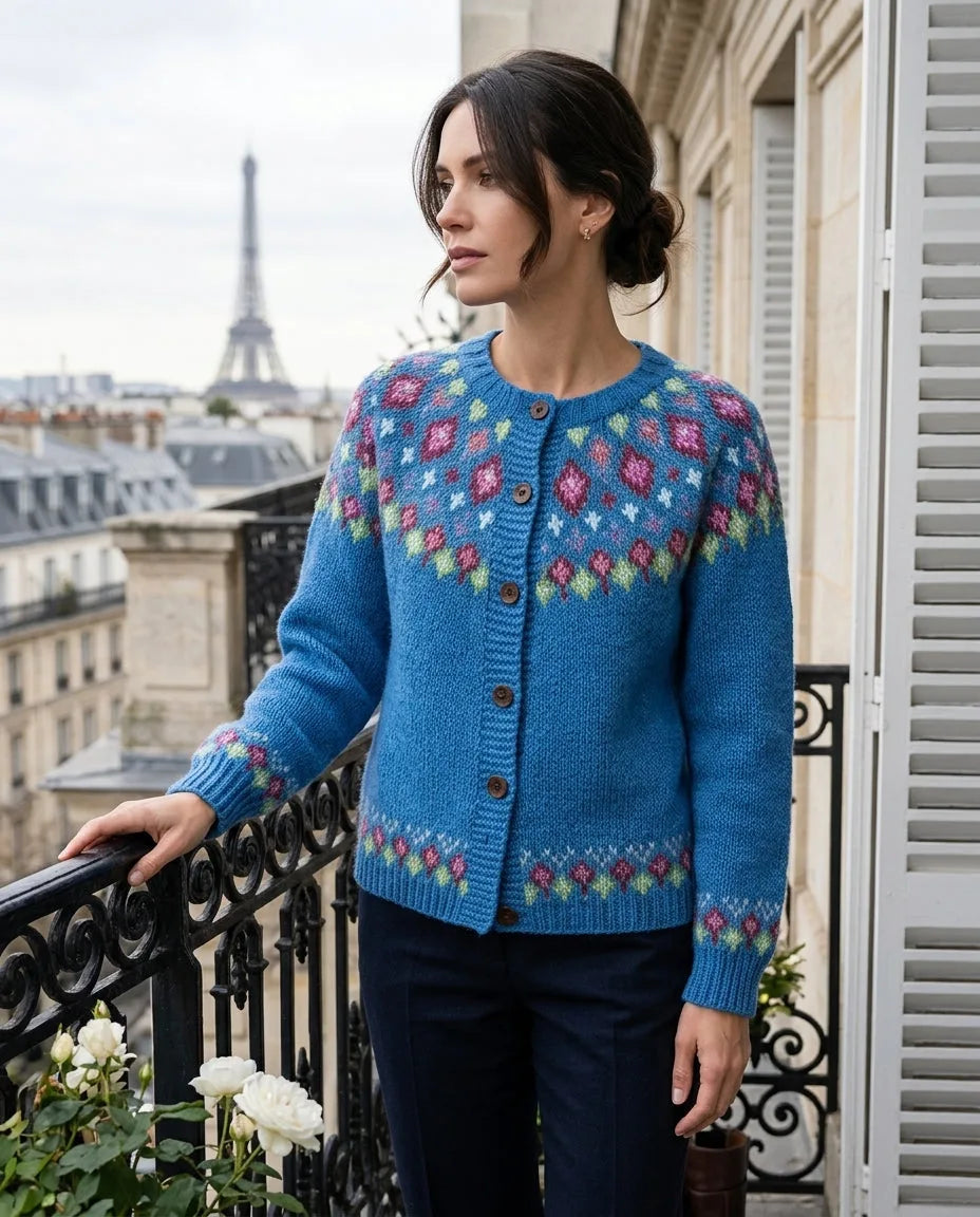 Woman in a blue fair isle cardigan with pink and green diamond yoke pattern, resting her hand on a wrought iron balcony railing