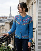 Woman in a blue fair isle cardigan with pink and green diamond yoke pattern, resting her hand on a wrought iron balcony railing
