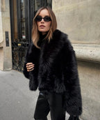 Woman wearing a cropped black faux fur coat with wide collar over black leather trousers on a Paris street