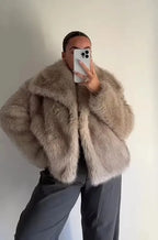 Front view of the faux fur coat showing the wide collar framing the neckline against sunglasses and dark lipstick