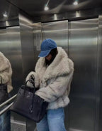 Woman holding a black handbag while wearing the oversized black faux fur coat on a cobbled street