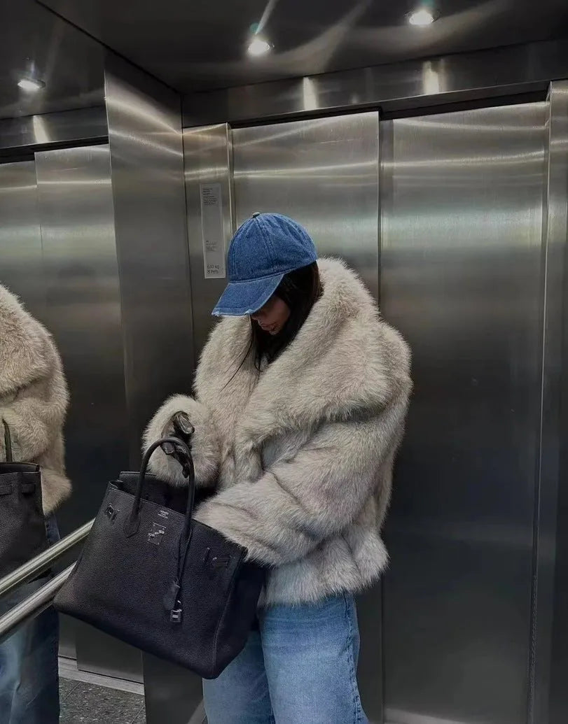 Woman holding a black handbag while wearing the oversized black faux fur coat on a cobbled street
