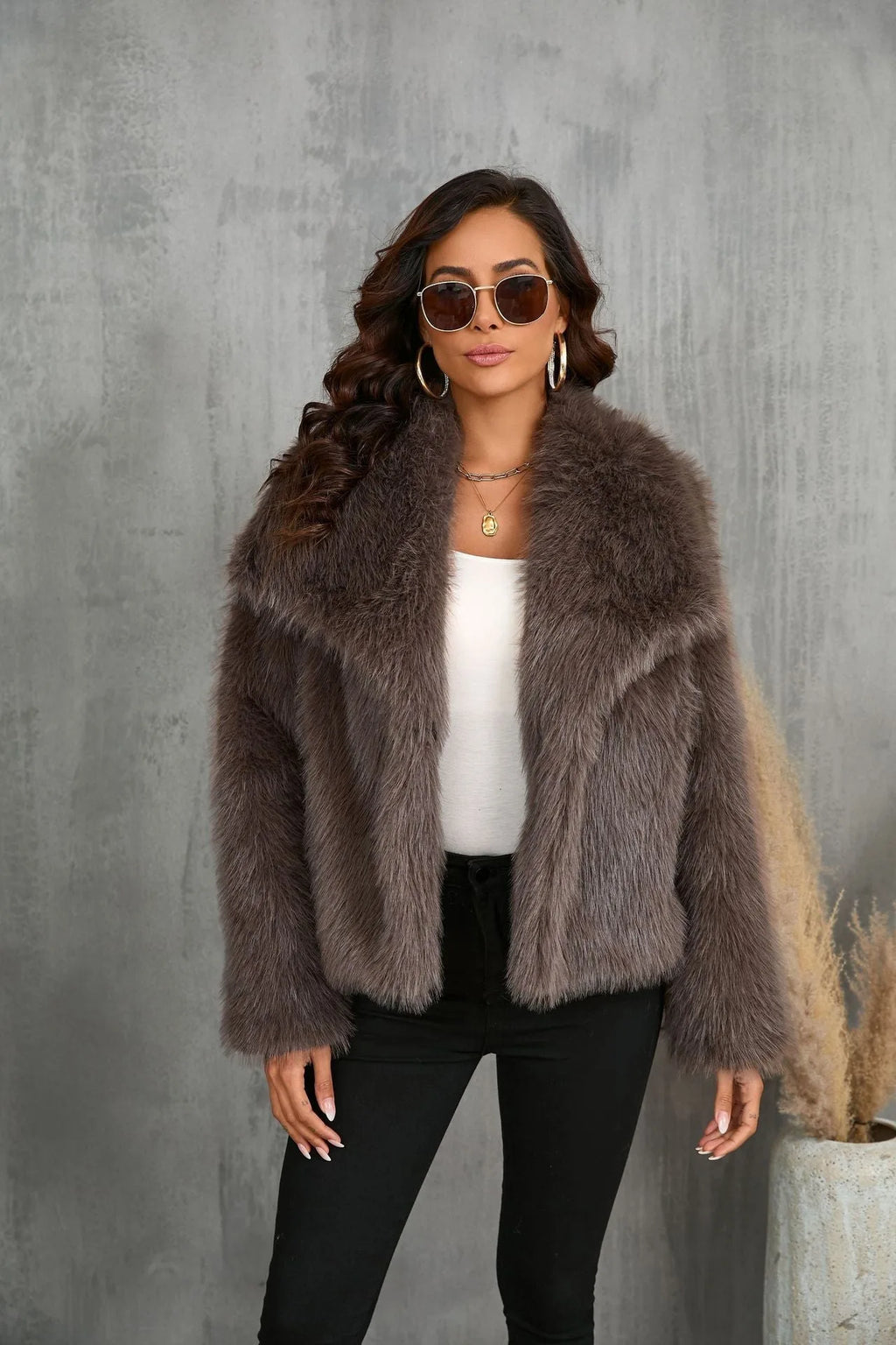 Wide shot of the model walking through a plaza wearing the black faux fur coat with a structured handbag