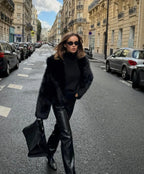 Model walking in a black shaggy faux fur coat paired with black leather trousers and a black tote bag