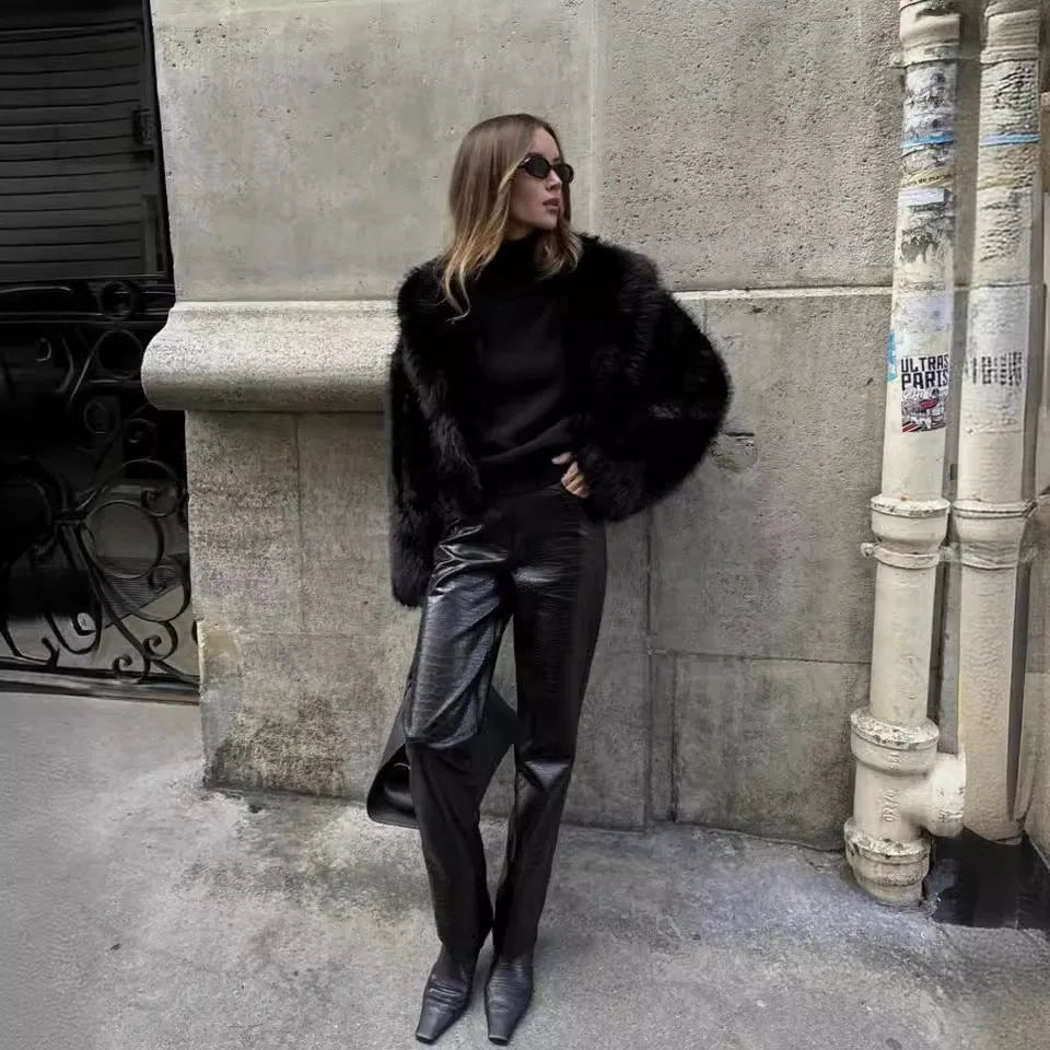 Side profile of the black faux fur coat's oversized collar and long sleeve against a stone wall