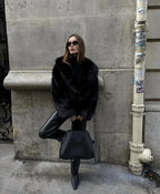 Woman leaning against a wall wearing the black faux fur coat with leather trousers and pointed boots