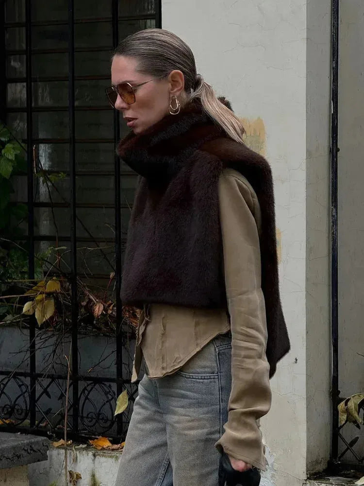 Model wearing a dark brown faux fur gilet with polo neck over a beige jumper and grey jeans