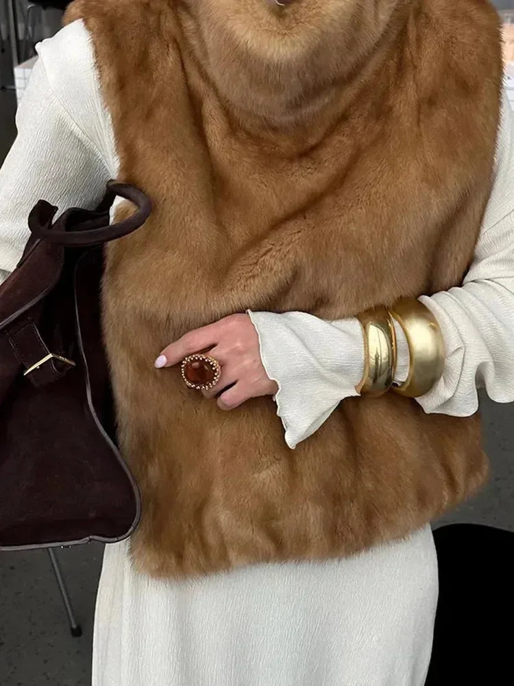 Close-up of a light brown faux fur gilet worn over a cream dress, styled with layered gold rings and bangles