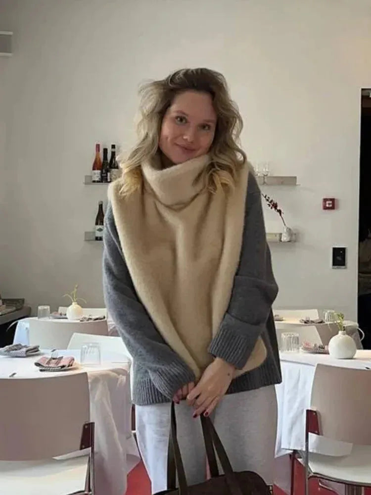 Model wearing a beige faux fur gilet draped over a grey jumper in a restaurant setting