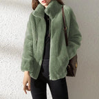 Front view of model wearing a sage green faux fur jacket with stand collar and zip fastening, paired with black jeans
