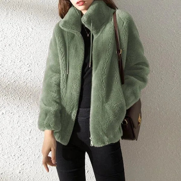 Front view of model wearing a sage green faux fur jacket with stand collar and zip fastening, paired with black jeans