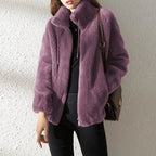 Model wearing a plum purple faux fur jacket with high collar, oversized sleeves and crossbody bag