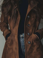 Detailed view of brown suede-effect trench coat front buttons and welt pockets against a black jumper