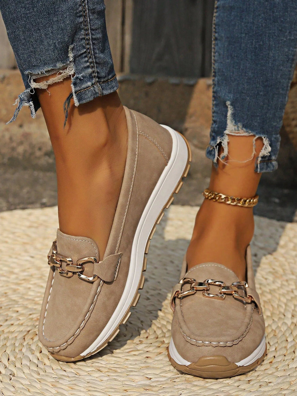 Close-up of khaki suede-look loafer with gold chain buckle detail, worn with ripped jeans on woven rug