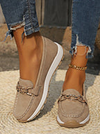 Close-up of khaki suede-look loafer with gold chain buckle detail, worn with ripped jeans on woven rug