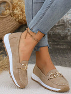 Light taupe suede loafer with gold buckle worn barefoot beside dried floral display
