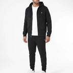 Man wearing black full-zip hooded tracksuit with white trainers in a relaxed everyday outfit