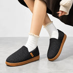 Side view of a woman's leg in a frilled white sock stepping into a black slip-on slipper with a tan sole