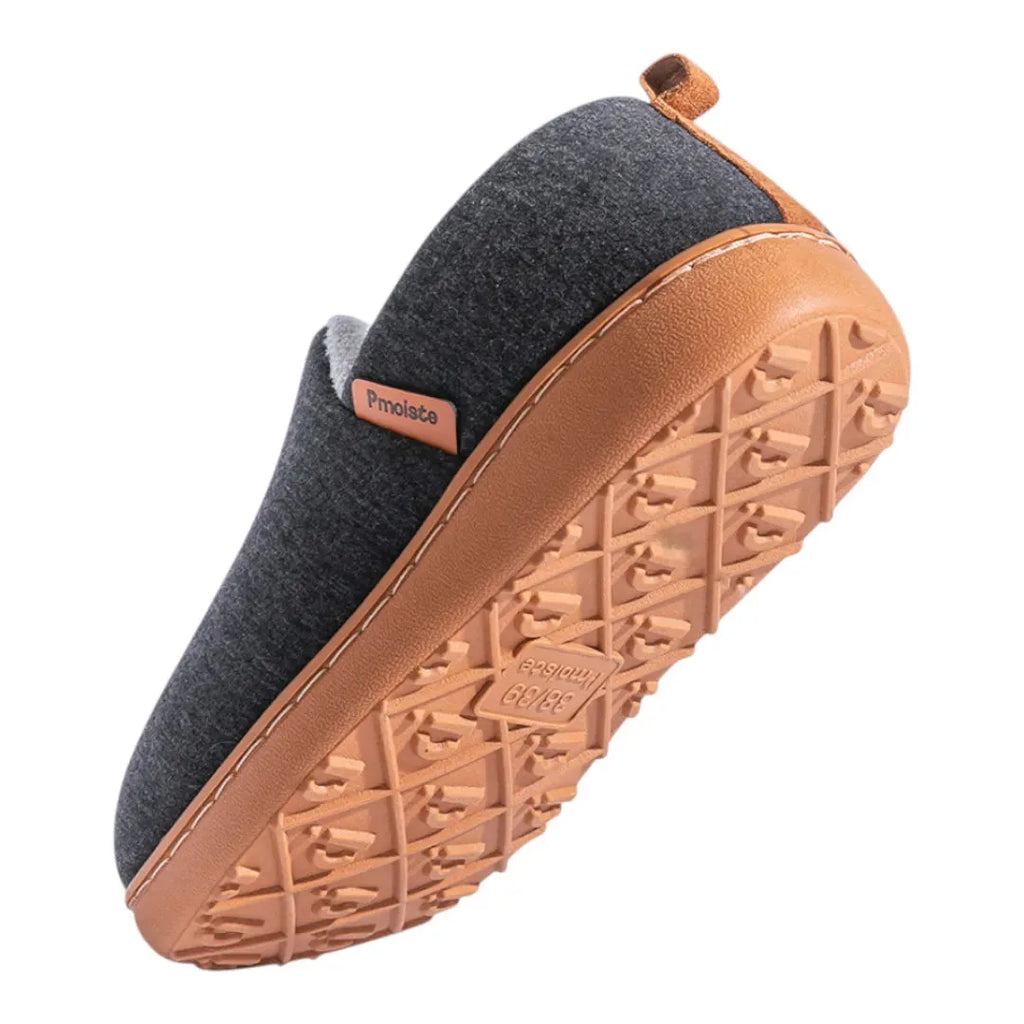 Top down angled shot of a dark charcoal slipper highlighting the brand tab and stitched tan sole edge