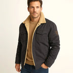 Man wearing a dark charcoal jacket with sherpa collar and dark denim trousers
