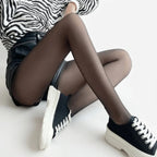 Close-up of sheer black thermal tights paired with a leather-look skater skirt and platform trainers