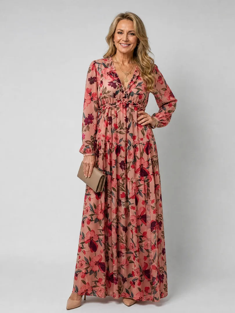 Woman wearing pink floral chiffon maxi dress with ruffled V-neck, tiered skirt and beige clutch bag